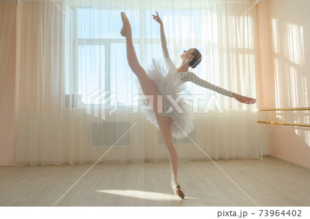 Beautiful ballerina in body and white tutu is training in a dance class. Young flexible dancer posing in pointe shoes. 73964402