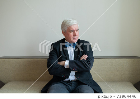 Displeased business man in suit and bow tie sits with his arms crossed on his chest. Displeased business man in suit and bow tie sits with his arms crossed on his chest. 73964446