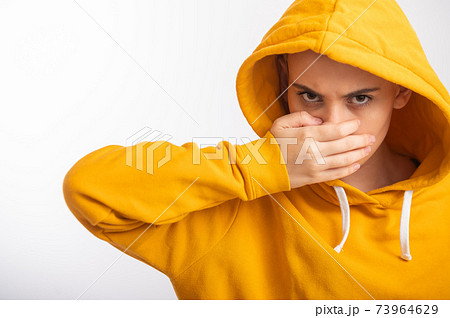 Young woman in ocher hood covers her face with hand on white background. Young woman in ocher hood covers her face with hand on white background. 73964629