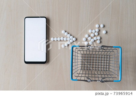 Online pharmacy. Arrow flu pills and a mini shopping basket next to a white screen mobile phone. Smartphone app for buying medicine. 73965914
