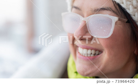 Smiling Caucasian woman stands on the balcony of a brick house in winter. Happy girl in ice-covered glasses on the street outdoors Smiling Caucasian woman stands on the balcony of a brick house in winter. Happy girl in ice-covered glasses on the street outdoors 73966420
