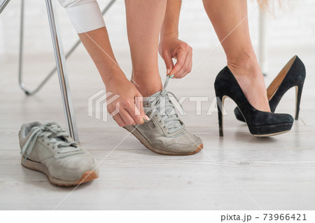 Close-up of a business woman taking off black high heel shoes and changing into comfortable sneakers. 73966421