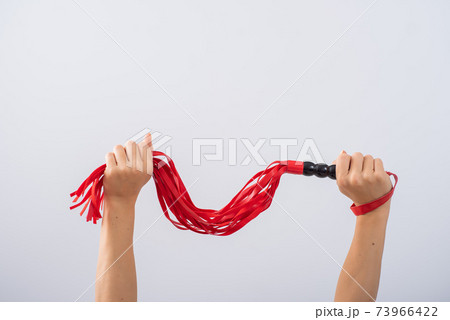Red leather whip in female hands on a white background. Copy space. Red leather whip in female hands on a white background. Copy space. 73966422