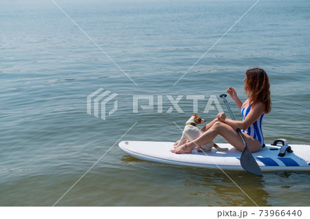 A woman is riding a sup surfboard with a dog on the lake. The girl goes in for water sports with her pet. 73966440