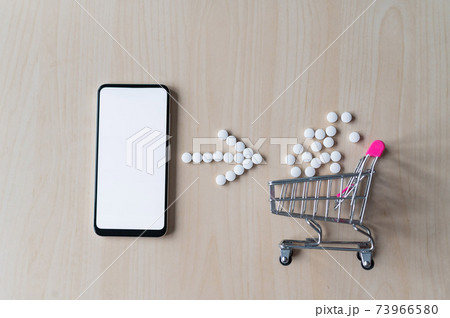 Online pharmacy concept. Buying medicine online over the phone. Delivery of pharmaceuticals. Mini trolley with tablets and smartphone with white blank screen. Online pharmacy concept. Buying medicine online over the phone. Delivery of pharmaceuticals. Mini trolley with tablets and smartphone with white blank screen. 73966580