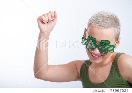 Portrait of a young Caucasian woman with a man's haircut in a green T-shirt and cheerful glasses on a white background. The girl celebrates st patrick's day 73967022