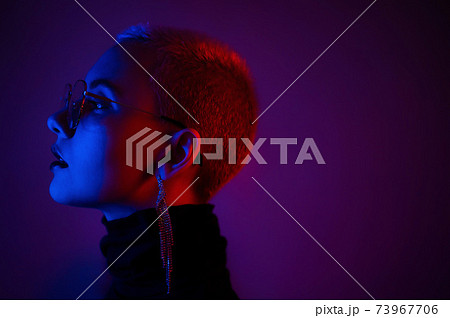 Close-up portrait of young blonde woman with short hair wearing glasses in neon light Close-up portrait of young blonde woman with short hair wearing glasses in neon light 73967706