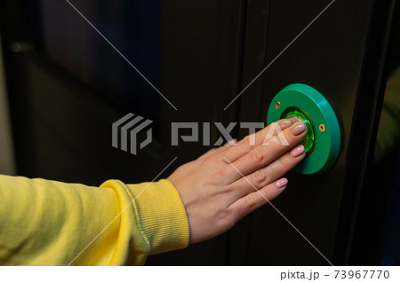 Button for opening doors on the train. Close-up of female hands on the green automatic door opener button 73967770