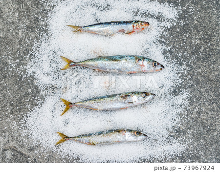 Whole raw organic mackerel fish with sea salt lying on a flat surface 73967924