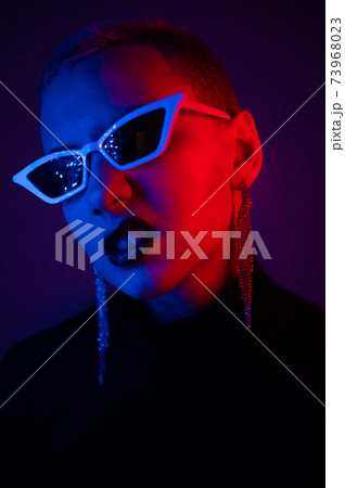 Portrait of a young woman with a short male haircut in sunglasses in neon light in the studio 73968023