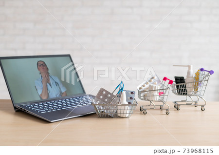 Online medicine and pharmacy concept. A female doctor conducts an online consultation and recommends medications. Mini trolley with tablets at the laptop. 73968115