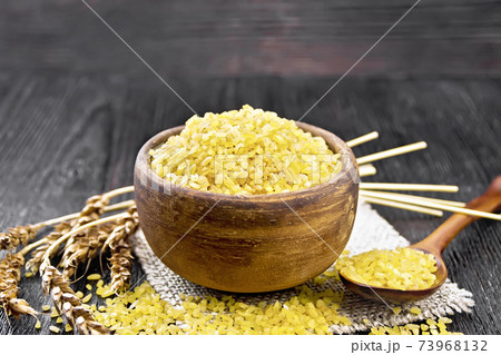 Bulgur in bowl on dark wooden board 73968132