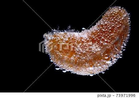 Mandarin slice in sparkling water isolated on black background Mandarin slice in sparkling water isolated on black background 73971996