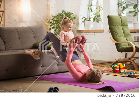 Young woman exercising fitness, aerobic, yoga at home, sporty lifestyle. Getting active with her child playing, home gym. 73972016