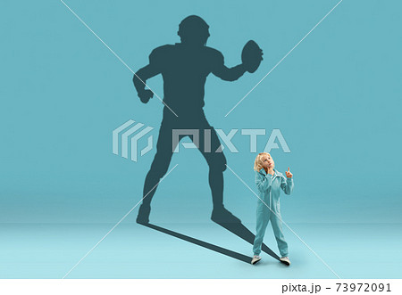 Childhood and dream about big and famous future. Conceptual image with boy and shadow of fit male american football player on blue background Childhood and dream about big and famous future. Conceptual image with boy and shadow of fit male american football player on blue background 73972091