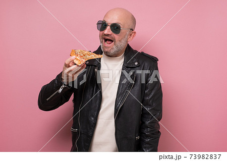Cheerful guy eating a pizza slice isolated on pink background 73982837