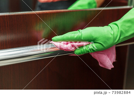 Antiviral disinfection with an aerosol sanitizer for elevator handrails, with female hands in gloves and a napkin. 73982884