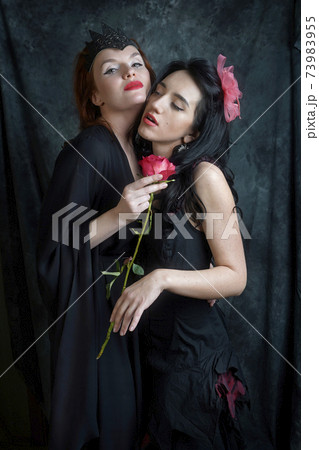 Two women are intoxicated by the fragrance of a red rose Two women are intoxicated by the fragrance of a red rose 73983955