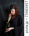 Woman in black dress sniffs red rose Woman in black dress sniffs red rose 73983957