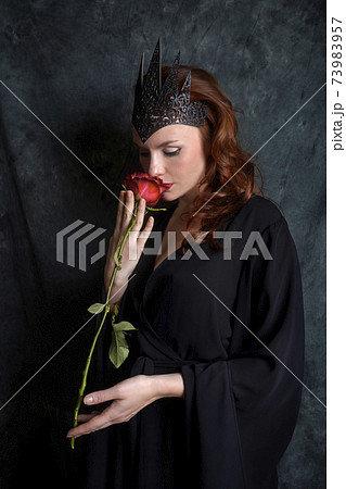 Woman in black dress sniffs red rose Woman in black dress sniffs red rose 73983957