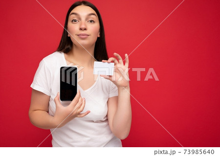 Self-confident attractive happy young brunette woman wearing casual white t-shirt isolated over red Self-confident attractive happy young brunette woman wearing casual white t-shirt isolated over red 73985640