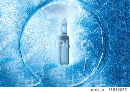 glass frozen ampoule with a virus vaccine on the texture of cold ice top view, background with backlight on the theme of pharmaceutical drugs from viral diseases. 73986077
