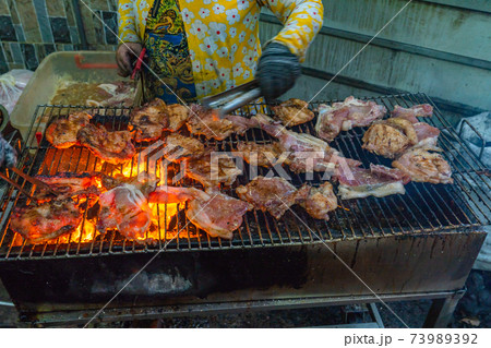 Woman grilling pork chop and ribs on flaming charcoal stove Woman grilling pork chop and ribs on flaming charcoal stove 73989392