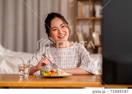 夜の食事しながらテレビを見る若い女性 73989587