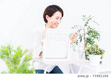 スマホを見ながらスキンケアをするミドル女性 73992168
