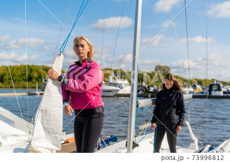 Two young blonde girls on a sunny summer day on a sailing boat are preparing for a river trip 73996812