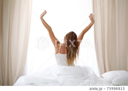 Woman stretching in bed after wake up, back view, entering a day happy and relaxed after good night sleep. Sweet dreams, good morning, new day, weekend, holidays concept 73996813