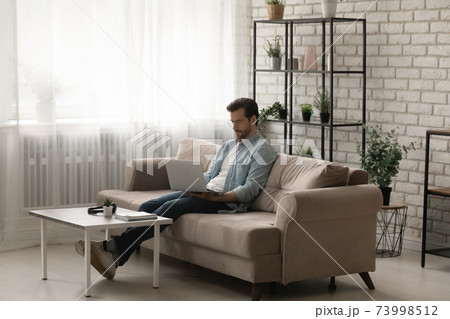 Serious man wearing glasses using laptop in modern living room 73998512