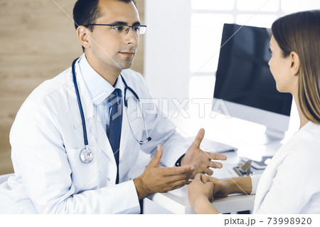 Doctor and patient discussing something while sitting at the desk in clinic. Concept of medicine and comfortable service in clinic 73998920