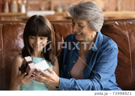 Close up smiling mature grandmother presenting gift to little girl 73998921
