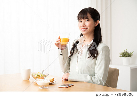 出勤前に朝食でオレンジジュースを飲む女性の写真素材