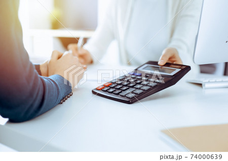 Accountant checking financial statement or counting by calculator income for tax form, hands closeup. Business woman sitting and working with colleague at the desk in office. Tax and Audit concept 74000639