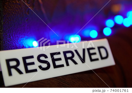 Plastic plaque with the inscription Reserved against the background of blue lights. Close-up, selective focus 74001761