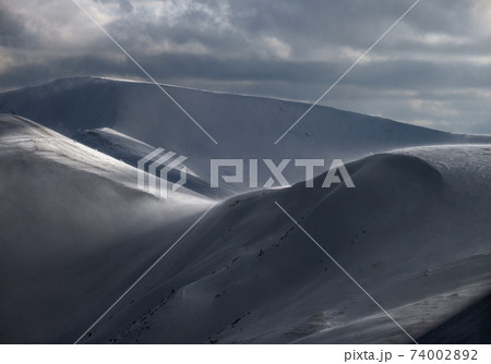 Snow covered winter mountains  in last evening sunlight. Magnificent windy dusk. 74002892
