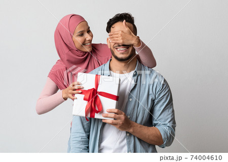 Loving muslim woman in hijab surprising her husband with gift box 74004610