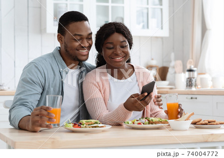 Happy African American Spouses Using Smartphone While Having Breakfast In Kitchen 74004772