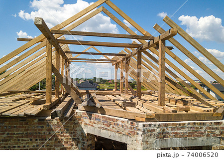 Aerial view of unfinished house with wooden roof frame structure under construction. 74006520
