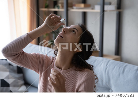 Head shot young caucasian woman using medical eyes drops. Head shot young caucasian woman using medical eyes drops. 74007533