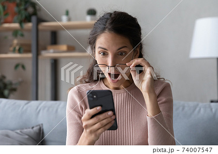 Emotional young woman looking at smartphone screen with opened mouth. Emotional young woman looking at smartphone screen with opened mouth. 74007547