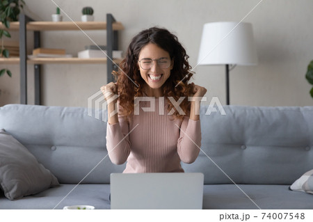 Overjoyed young woman in eyeglasses celebrating online lottery win. Overjoyed young woman in eyeglasses celebrating online lottery win. 74007548