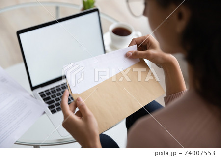Close up young woman opening envelope with letter. 74007553
