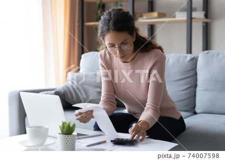 Focused smart millennial woman in eyeglasses busy with financial paperwork. Focused smart millennial woman in eyeglasses busy with financial paperwork. 74007598