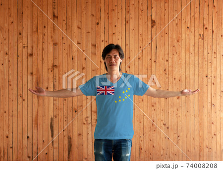 Man wearing Tuvalu flag color shirt and standing with arms wide open on the wooden wall background. Man wearing Tuvalu flag color shirt and standing with arms wide open on the wooden wall background. 74008208