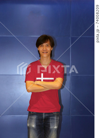 Man wearing Denmark flag pattern shirt and cross one's arm on the blue wall background, 74008209