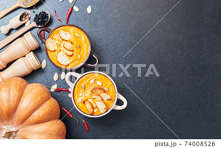 pumpkin cream soup with croutons on a black table with spices 74008526