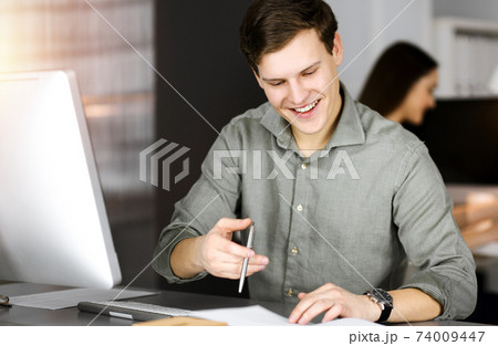 Young businessman working on his computer sitting at the desk in office. Headshot portrait of a man 74009447
